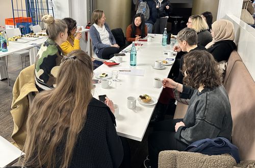 Foto vom Netzwerktreffen. 9 Frauen sitzen an einem Tisch und hören einer Frau gespannt zu