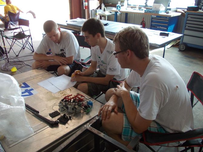 Tim Schlinkmann (links) erklärt zusammen mit Matthias Drossel(rechts) einem Teammitglied von Umicore, wie mit Hilfe von Checklisten beim Solarcar Fehler vermieden werden können.