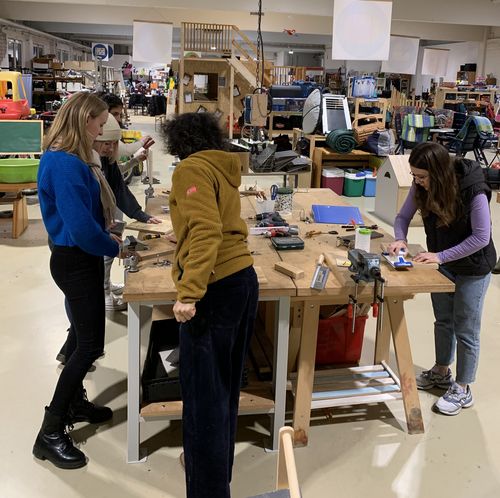 Foto vom Upcycling Workshop. 4 Teilnehmerinnen stehen um einen Werktisch und arbeiten an ihren Produkten.
