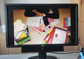 Monitor auf dem eine resignierte Studentin vor einem chaotischen Schreibtisch sitzt
