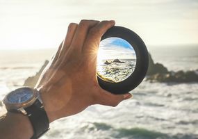 Auf einem Monitor ist das Bild einer Hand mit einer Linse, die das Bild einer Insel klar zeigt