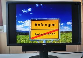 Monitor, auf dem ein Ortsausgangsschild mit "Anfangen" und durchgestrichen "Aufschieben"zu sehen ist
