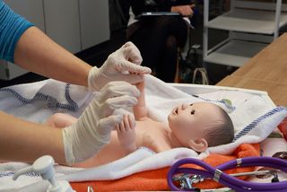 Hebamme demonstriert Babypflege an Puppe