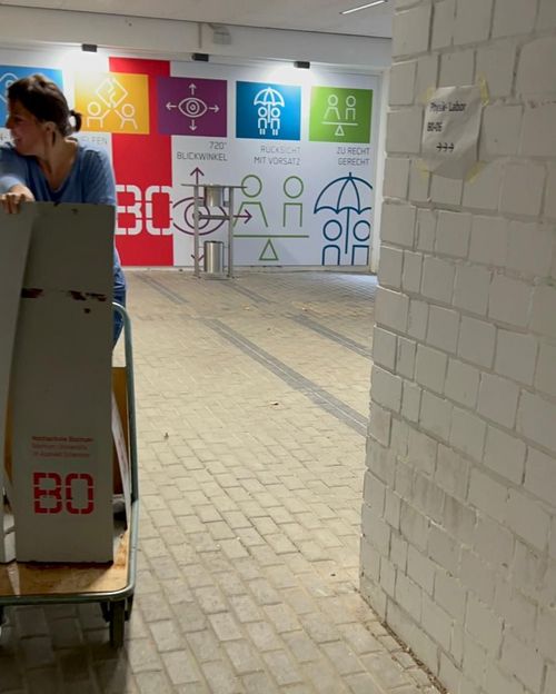 auf einem Handwagen werden graue Aufsteller um eine Ecke im Untergeschoss des Zentralcampus gefahren