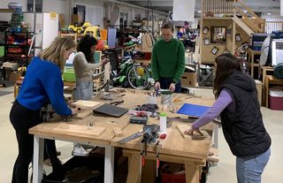 Foto vom Upcycling Workshop. 4 Teilnehmerinnen stehen um einen Werktisch und arbeiten an ihren Produkten