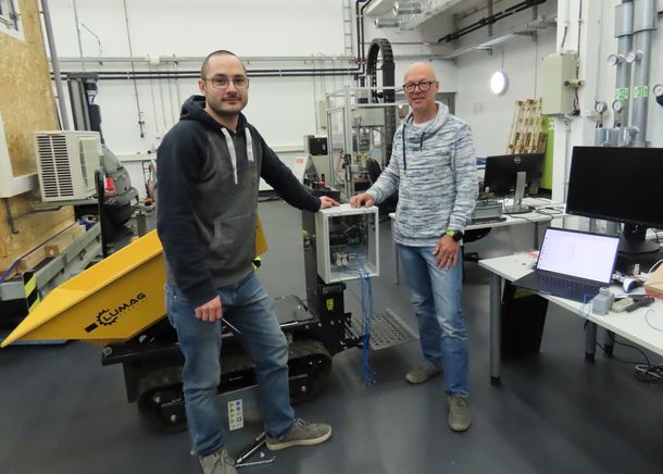 Student Kevin Koster hat an einen industriellen Dumper einen Rechner montiert, über den der Dumper autonom gesteuert werden kann. Student Kevin Koster und Prof. Dr. Dietmar Gerhardt stehen vor dem Dumper.