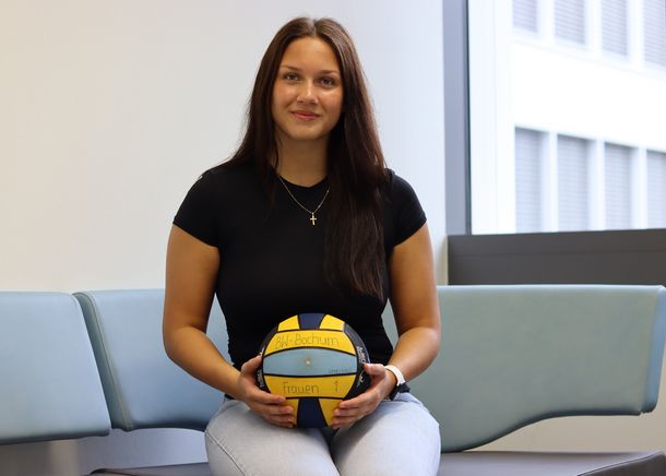 Die Studentin sitzt auf einer Bank und hält einen Wasserball in den Händen.