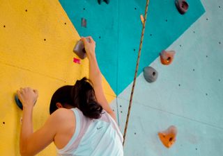 Eine Frau klettert gesichert an einer Kletterwand
