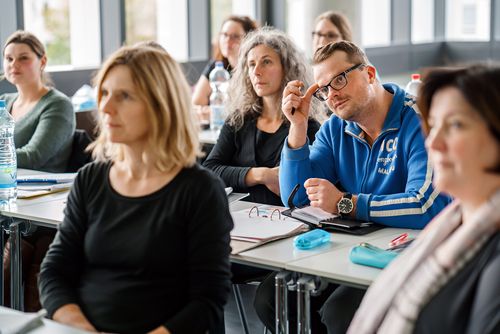 Seminarsituation mit Fokus auf einen Mann, der nachdenklich guckt.