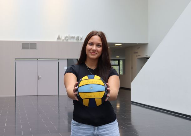 Die Studentin hält im Atrium der Hochschule einen Wasserball in den Händen.