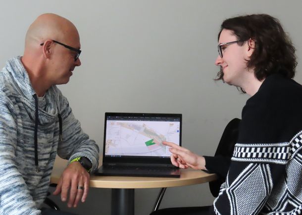 Student Tobias Hensel hat eine Weboberfläche programmiert, über die exakt ausgewählt werden kann in welchem Gebiet sich Drohne und Dumper bei ihrer Wiesenarbeit bewegen dürfen. Student Tobias Hensel zeigt auf eine programmierte Weboberfläche, über die exakt ausgewählt werden kann in welchem Gebiet sich Drohne und Dumper bei ihrer Wiesenarbeit bewegen dürfen. Prof. Dr. Dietmar Gerhardt sitzt ihm gegenüber und schaut ebenfalls auf die Weboberfläche.