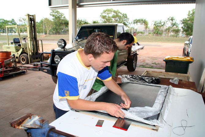 Christoph Scheithauer und Yavuz Apaydin laminieren eine Kohlefaserplatte. Um die Aerodynamik der Räder weiter zu verbessern, wird aus dieser Platte eine Speichenabdeckung gefertigt.