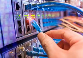 Ein Mann arbeitet in einem Netzwerkserverraum mit einem Glasfaser-Hub für digitale Kommunikation und Internet