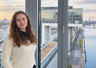 Ein Portrait von MAAT-Alumna Dorothea Kretschmar aus einem Gebäude mit Aussicht auf den Rhein.
