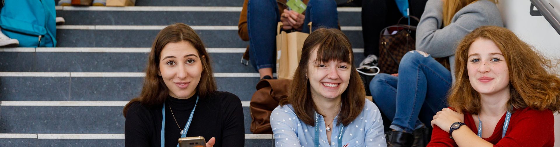 Auf diesem Bild sieht man drei Studentinnen, die auf einer Treppe sitzen.