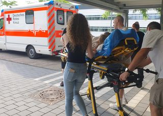 Gemeinsames Simulationstraining am Gesundheitscampus: Studierende trainieren mit angehenden Notfallsanitätskräften die optimale Zusammenarbeit bei seltenen Geburtskomplikationen. Auf einer Fahrtrage wird die Gebärende zum Rettungswagen vor dem Hochschulgebäude gebracht.